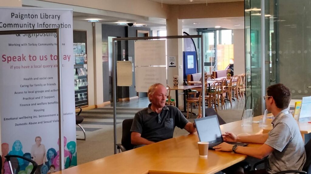 Jack Watts (right), Engaging Communities South West Administrator, manning the new Community Hub at Paignton Library and speaking with a member of the public